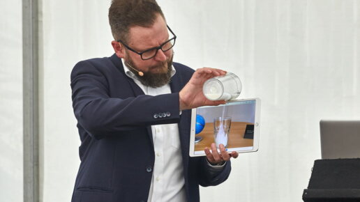 Der Magier macht eine Show mit einem IPad und mit einem vollem Glas.